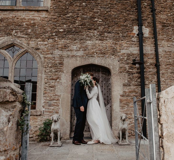 Bride in Homemade Wedding Dress with Long Sleeves and Groom in Navy Reiss Suit Standing Outside Rook Lane Wedding Venue in Somerset