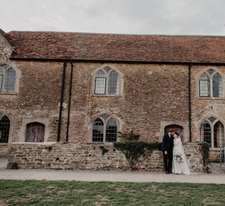 Bride in Homemade Wedding Dress with Long Sleeves and Groom in Navy Reiss Suit Standing Outside Rook Lane Wedding Venue in Somerset