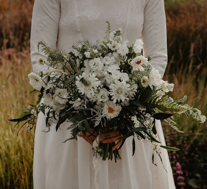 Bride in Homemade Wedding Dress with Long Sleeves Holding White and Green Wedding Bouquet