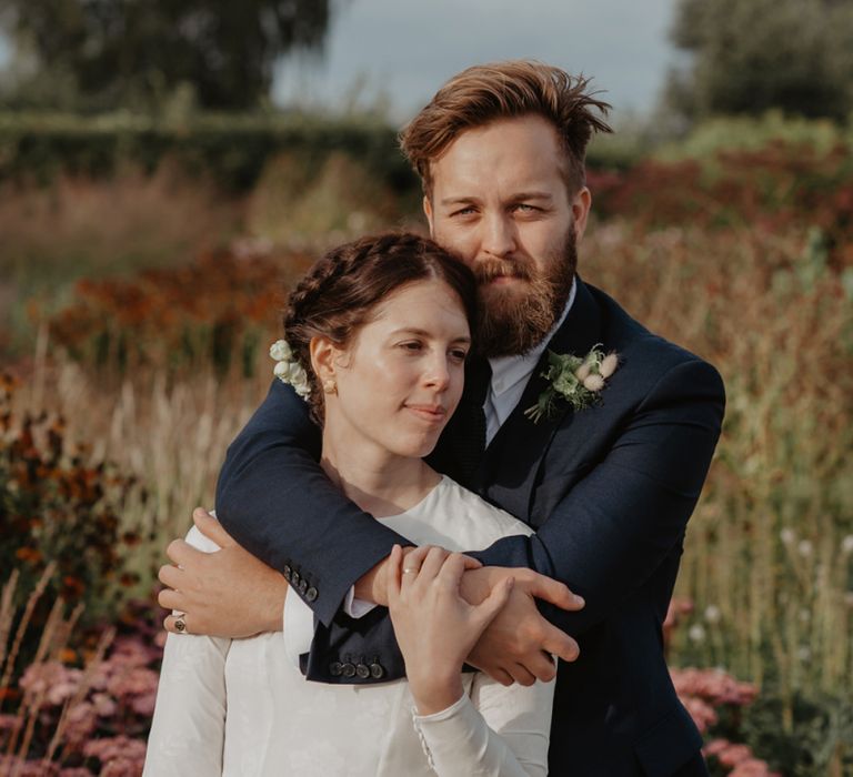 Bride in Homemade Wedding Dress with Long Sleeves and Groom in Navy Reiss Suit Embracing