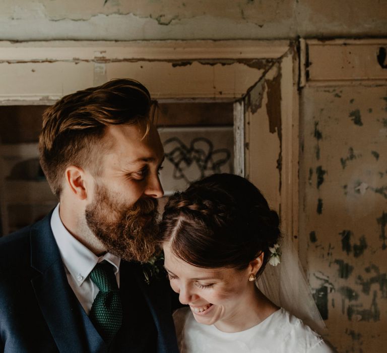 Groom in Three-Piece Navy Reiss Suit Embracing Bride in Homemade Wedding Dress with Long Sleeves