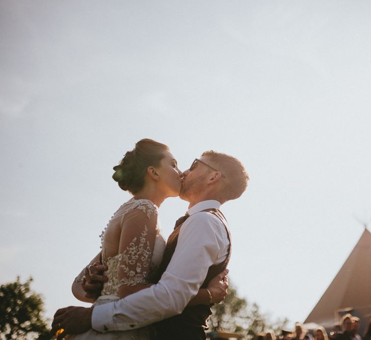 Bride and groom kissing with tipi in the background