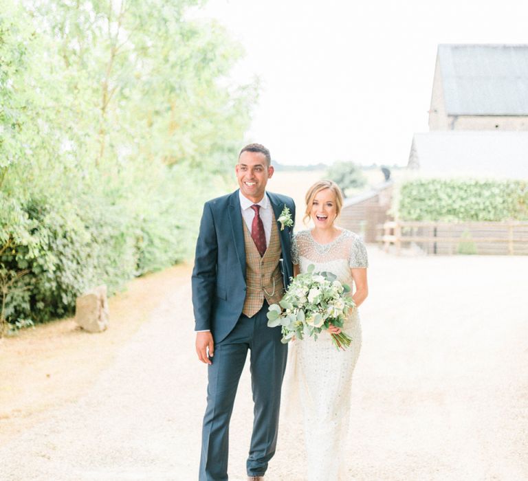 Happy Bride in Beaded Wedding Dress and Groom in Dark Suit &amp; Check Waistcoat