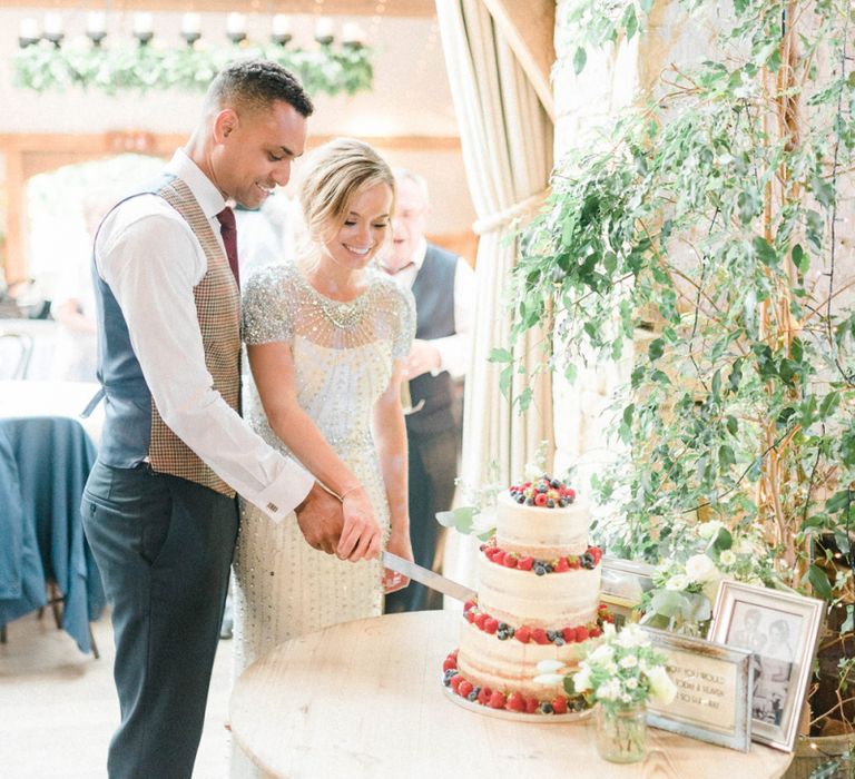 Bride in Beaded Wedding Dress and Groom in Dark Suit &amp; Check Waistcoat Cutting the Wedding Cake