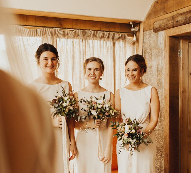 Bridesmaids in blush dresses see bride in wedding dress for first time