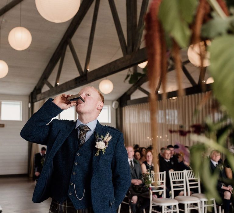 Groom in tartan kilt and wool jacket drinking from a hip flask at the altar