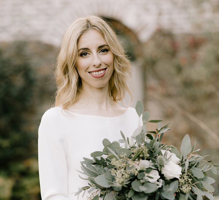 Bride in Long Sleeved Andrea Hawkes Dress with Bateau Neck and Low V-Back with Buttons | Bridal Bouquet with Eucalyptus, White Roses, White and Blue Thistles and Ferns | Emerald Green Bridesmaid Dress for a Winter Wedding at Middleton Lodge | Georgina Harrison Photography