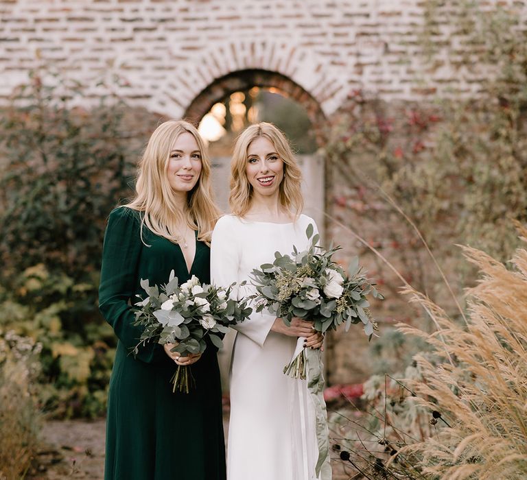 Bride in Long Sleeved Andrea Hawkes Dress with Bateau Neck and Low V-Back with Buttons | Bridesmaid in Forest Green Reformation Dress with Long Sleeves | Wedding Bouquets with Eucalyptus, White Roses, White and Blue Thistles and Ferns | Emerald Green Bridesmaid Dress for a Winter Wedding at Middleton Lodge | Georgina Harrison Photography