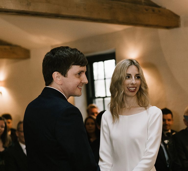 Bride in Long Sleeved Andrea Hawkes Dress with Bateau Neck and Low V-Back with Buttons | Groom in Navy Three-Piece Suit from Suit Supply with Green Tie | Emerald Green Bridesmaid Dress for a Winter Wedding at Middleton Lodge | Georgina Harrison Photography