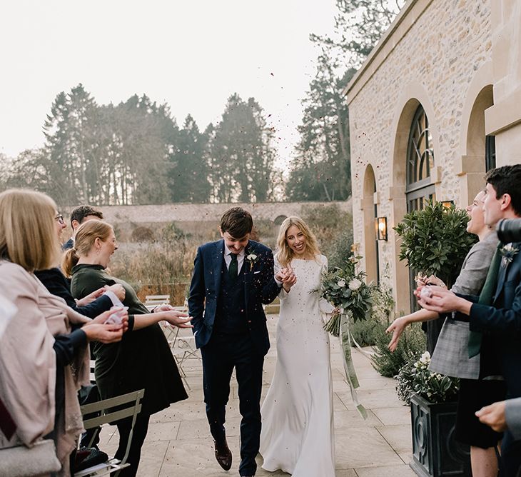 Bride in Long Sleeved Andrea Hawkes Dress with Bateau Neck and Low V-Back with Buttons | Groom in Navy Three-Piece Suit from Suit Supply with Green Tie | Bridal Bouquet with Eucalyptus, White Roses, White and Blue Thistles and Ferns | Emerald Green Bridesmaid Dress for a Winter Wedding at Middleton Lodge | Georgina Harrison Photography