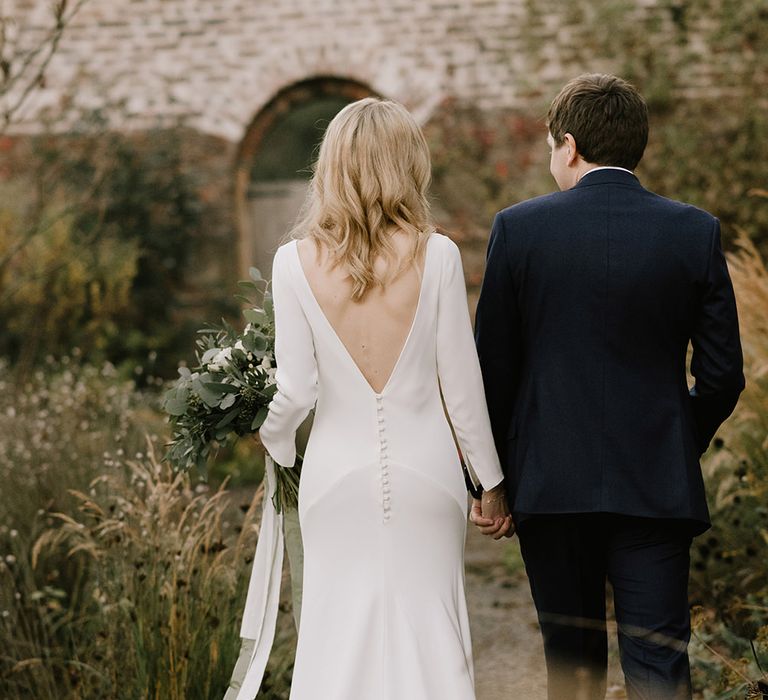 Bride in Long Sleeved Andrea Hawkes Dress with Bateau Neck and Low V-Back with Buttons | Groom in Navy Three-Piece Suit from Suit Supply with Green Tie | Bridal Bouquet with Eucalyptus, White Roses, White and Blue Thistles and Ferns | Emerald Green Bridesmaid Dress for a Winter Wedding at Middleton Lodge | Georgina Harrison Photography