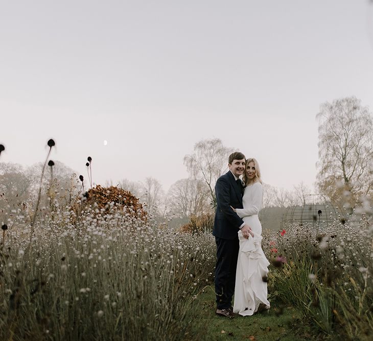 Bride in Long Sleeved Andrea Hawkes Dress with Bateau Neck and Low V-Back with Buttons | Groom in Navy Three-Piece Suit from Suit Supply with Green Tie | Emerald Green Bridesmaid Dress for a Winter Wedding at Middleton Lodge | Georgina Harrison Photography