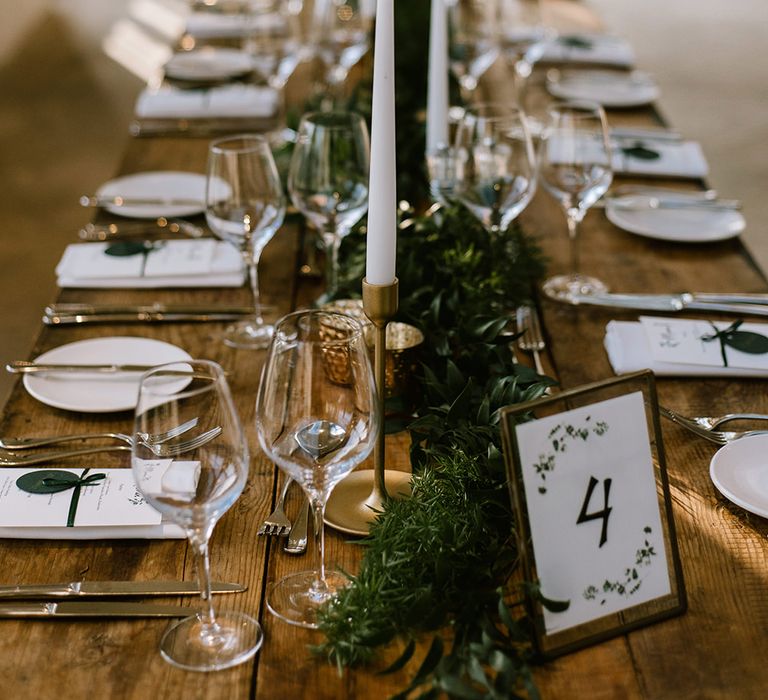 Wooden Banquet Tables | Foliage Table Runners | White Tapered Candles | Gold Candlesticks | Gold Tea Light Holders | Gold Framed Table Number | Emerald Green Bridesmaid Dress for a Winter Wedding at Middleton Lodge | Georgina Harrison Photography