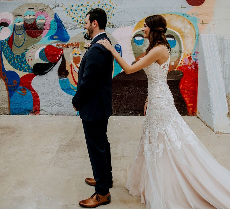 First Look Photo | Bride in Sleeveless High-Neck Stella York Gown with Lace Overlay and Gold Underskirt | Groom in Navy Suit and Floral Tie | Rifle Paper Co. Trainers for Informal Wedding in Fort Worth, Texas | Paul &amp; Nanda Photography