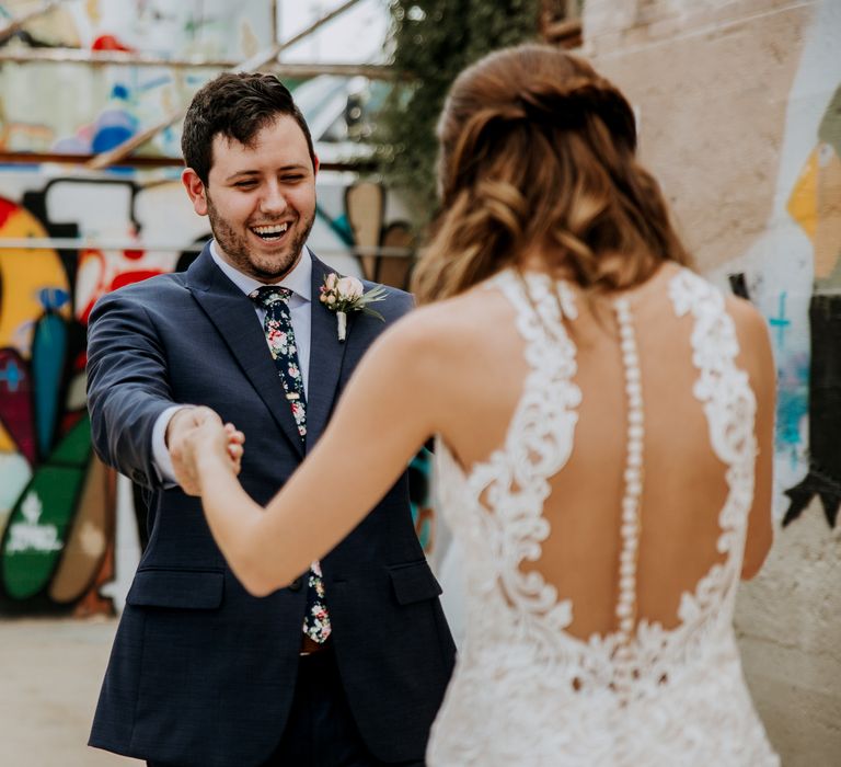 First Look Photo | Bride in Sleeveless High-Neck Stella York Gown with Lace Overlay and Gold Underskirt | Groom in Navy Suit and Floral Tie | Rifle Paper Co. Trainers for Informal Wedding in Fort Worth, Texas | Paul &amp; Nanda Photography