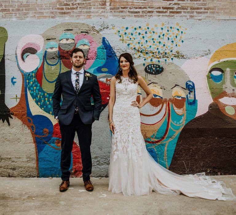 First Look Photo | Bride in Sleeveless High-Neck Stella York Gown with Lace Overlay and Gold Underskirt | Half Up Half Down Wedding Hair | Bride Wearing Red Lipstick | Groom in Navy Suit and Floral Tie | Rifle Paper Co. Trainers for Informal Wedding in Fort Worth, Texas | Paul &amp; Nanda Photography