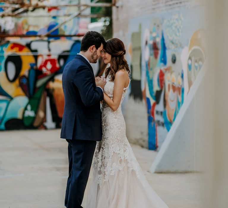 First Look Photo | Bride in Sleeveless High-Neck Stella York Gown with Lace Overlay and Gold Underskirt | Half Up Half Down Wedding Hair | Bride Wearing Red Lipstick | Groom in Navy Suit and Floral Tie | Rifle Paper Co. Trainers for Informal Wedding in Fort Worth, Texas | Paul &amp; Nanda Photography