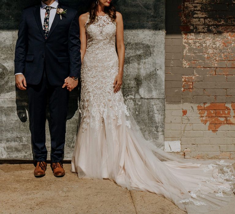 First Look Photo | Bride in Sleeveless High-Neck Stella York Gown with Lace Overlay and Gold Underskirt | Groom in Navy Suit and Floral Tie | Rifle Paper Co. Trainers for Informal Wedding in Fort Worth, Texas | Paul &amp; Nanda Photography