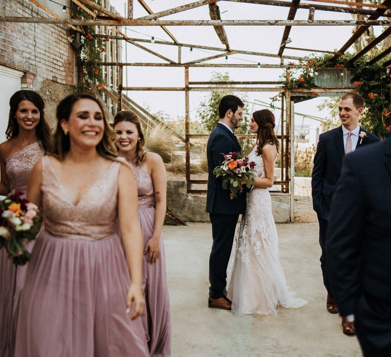 First Look Photo | Bride in Sleeveless High-Neck Stella York Gown with Lace Overlay and Gold Underskirt | Half Up Half Down Wedding Hair | Groom in Navy Suit and Floral Tie | Colourful Bridal Bouquet of Pink, Orange and White Flowers with Ferns, Eucalyptus and Greenery | Bridesmaids in Pink Dresses with Lace Bodice | Groomsmen in Navy Suits and Silk Blush Ties | Rifle Paper Co. Trainers for Informal Wedding in Fort Worth, Texas | Paul &amp; Nanda Photography