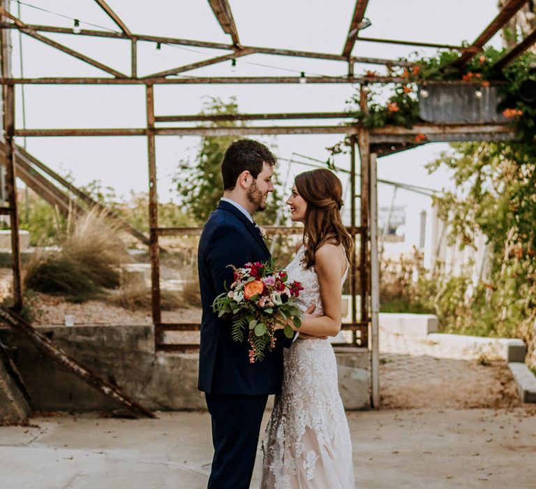 First Look Photo | Bride in Sleeveless High-Neck Stella York Gown with Lace Overlay and Gold Underskirt | Half Up Half Down Wedding Hair | Groom in Navy Suit and Floral Tie | Colourful Bridal Bouquet of Pink, Orange and White Flowers with Ferns, Eucalyptus and Greenery | Rifle Paper Co. Trainers for Informal Wedding in Fort Worth, Texas | Paul &amp; Nanda Photography