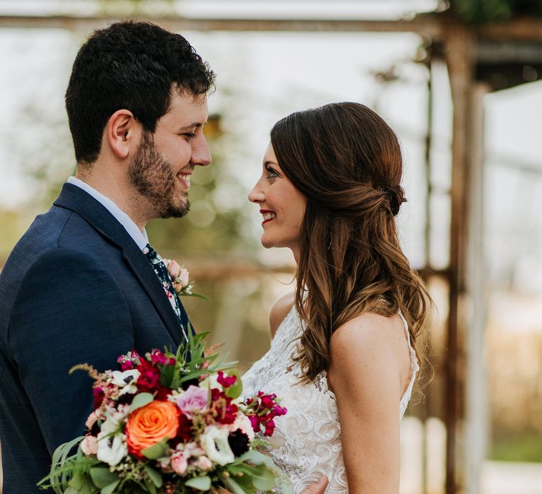 First Look Photo | Bride in Sleeveless High-Neck Stella York Gown with Lace Overlay and Gold Underskirt | Half Up Half Down Wedding Hair | Groom in Navy Suit and Floral Tie | Colourful Bridal Bouquet of Pink, Orange and White Flowers with Ferns, Eucalyptus and Greenery | Rifle Paper Co. Trainers for Informal Wedding in Fort Worth, Texas | Paul &amp; Nanda Photography