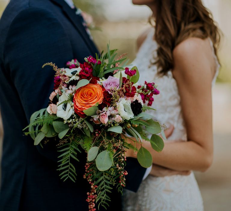 First Look Photo | Bride in Sleeveless High-Neck Stella York Gown with Lace Overlay and Gold Underskirt | Half Up Half Down Wedding Hair | Groom in Navy Suit and Floral Tie | Colourful Bridal Bouquet of Pink, Orange and White Flowers with Ferns, Eucalyptus and Greenery | Rifle Paper Co. Trainers for Informal Wedding in Fort Worth, Texas | Paul &amp; Nanda Photography