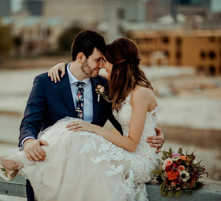 Bride in Sleeveless High-Neck Stella York Gown with Lace Overlay and Gold Underskirt | Blush Rifle Paper Co. Trainers with Pink Flowers and White Laces | Half Up Half Down Wedding Hair | Groom in Navy Suit and Floral Tie | Pink Buttonhole | Colourful Bridal Bouquet of Pink, Orange and White Flowers with Ferns, Eucalyptus and Greenery | Rifle Paper Co. Trainers for Informal Wedding in Fort Worth, Texas | Paul &amp; Nanda Photography