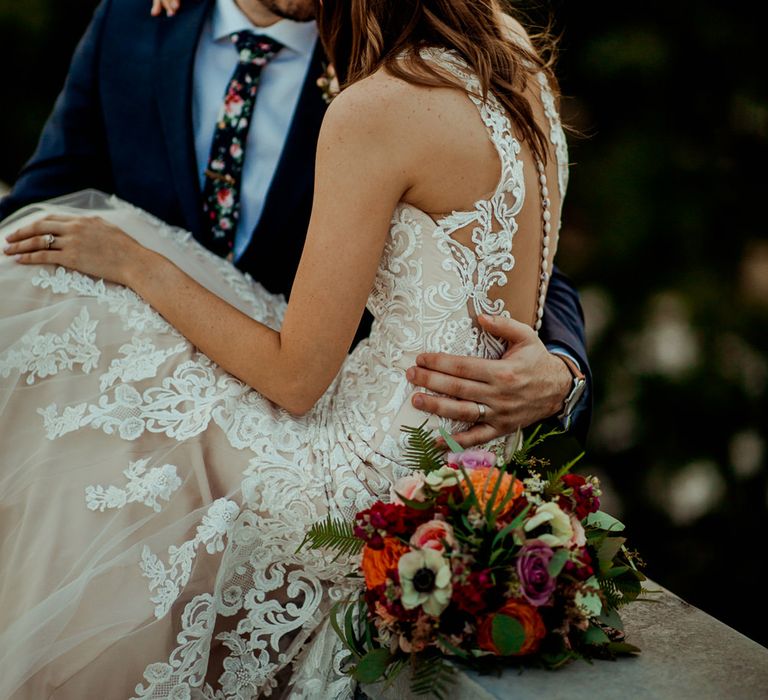 Bride in Sleeveless High-Neck Stella York Gown with Lace Overlay and Gold Underskirt | Half Up Half Down Wedding Hair | Groom in Navy Suit and Floral Tie | Pink Buttonhole | Colourful Bridal Bouquet of Pink, Orange and White Flowers with Ferns, Eucalyptus and Greenery | Rifle Paper Co. Trainers for Informal Wedding in Fort Worth, Texas | Paul &amp; Nanda Photography