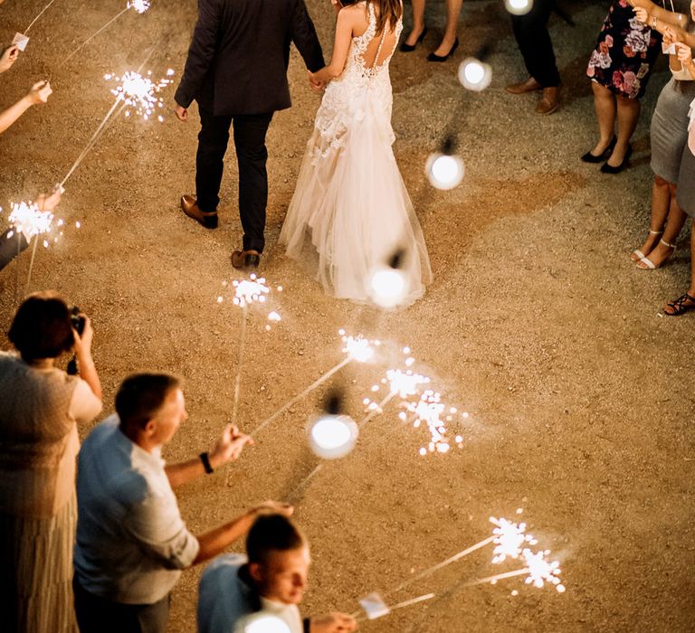 Sparkler Send Off | Bride in Sleeveless High-Neck Stella York Gown with Lace Overlay and Gold Underskirt | Groom in Navy Suit and Floral Tie | Festoon Lights | Rifle Paper Co. Trainers for Informal Wedding in Fort Worth, Texas | Paul &amp; Nanda Photography