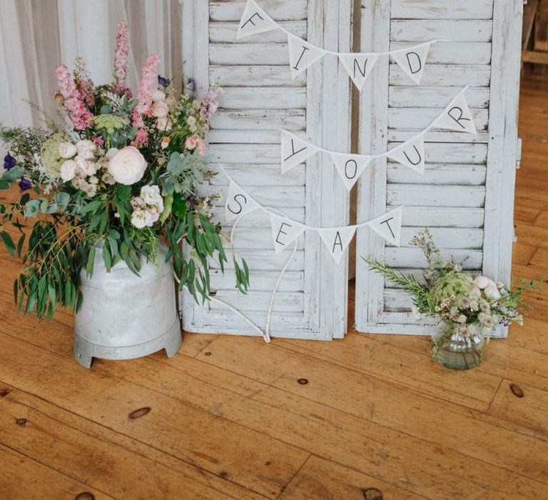 DIY wedding decor with find your seat wedding bunting and flowers in milk churn