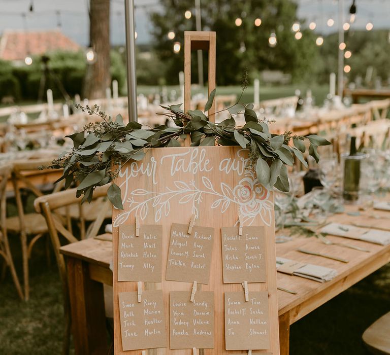 Wooden Table Plan with Greenery Decor | Festoon Lit Outdoor Boho Wedding at Chateau le Tour, France | Adam and Grace Photography | Head and Heart Films