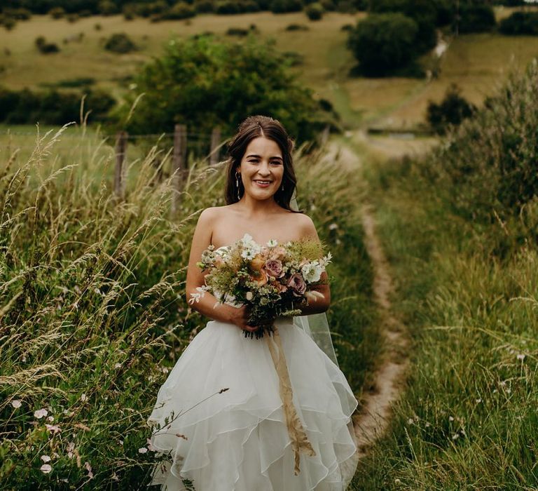 Bride clutching bouquet wearing layered wedding dress