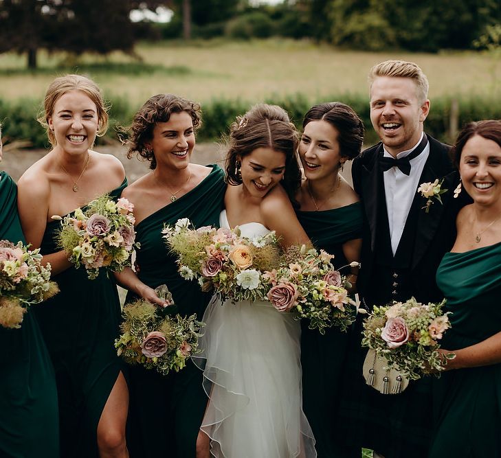 Bride in layered wedding dress with bridesmaids in emerald green dresses