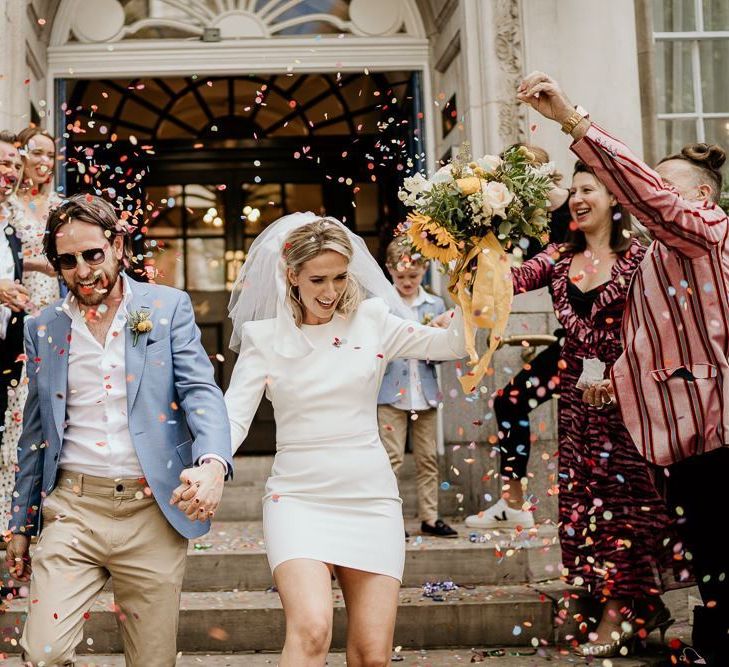 Confetti exit with bride in short wedding dress and groom in blue blazer and chinos