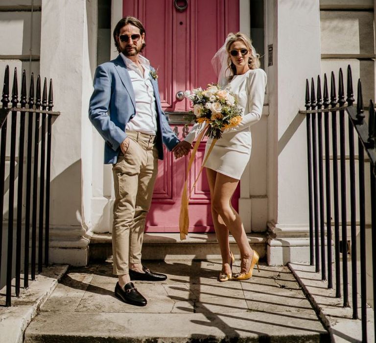 Stylish bride and groom standing on a doorstep with LOVE sign and pink door