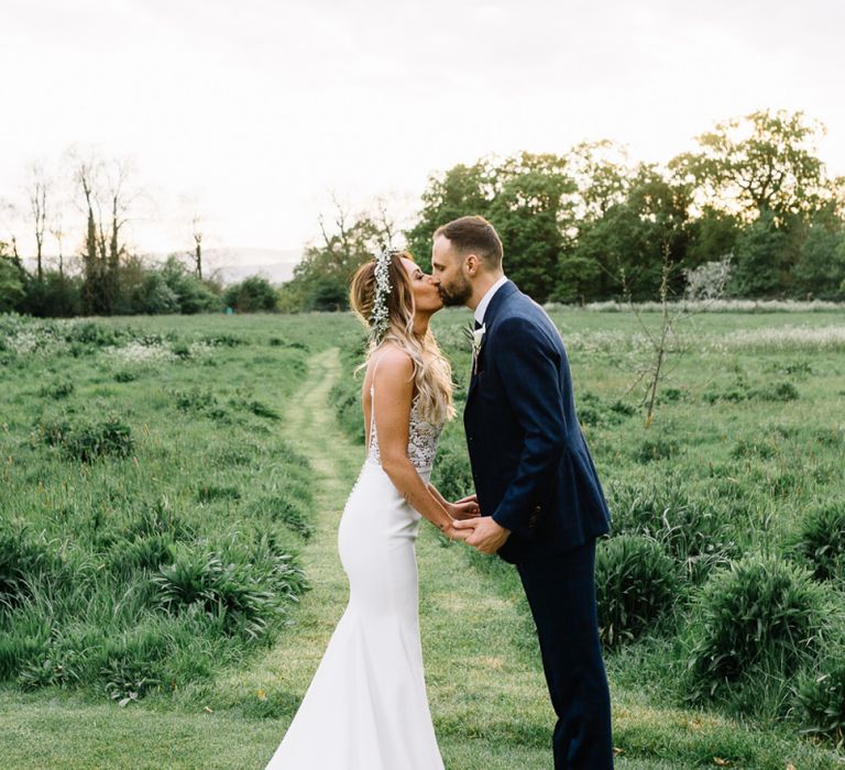 Bride in Fitted Mikaella Wedding Dress  and Flower Crown and Groom in Bespoke Navy Check Suit Kissing