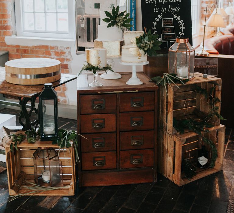 Wedding Cake Display | Gold Foil &amp; White Wedding Cakes | Chalkboard Wedding Sign | Wooden Crates | Pink Roll Top Booze Bath and Copper &amp; Perspex Wedding Decor at Industrial Venue The West Mill | Rosie Kelly Photography