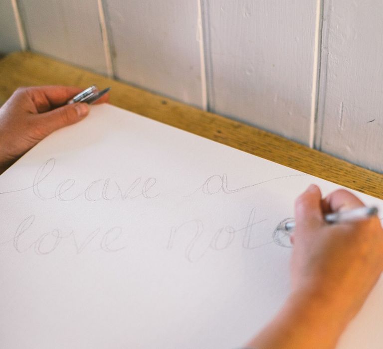 Person writing the words 'Leave a love note' onto a box canvas in silver pen