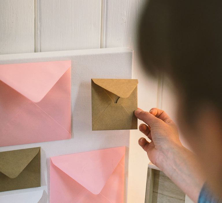 Person sticking a brown kraft envelope onto a white canvas as part of a DIY wedding card table