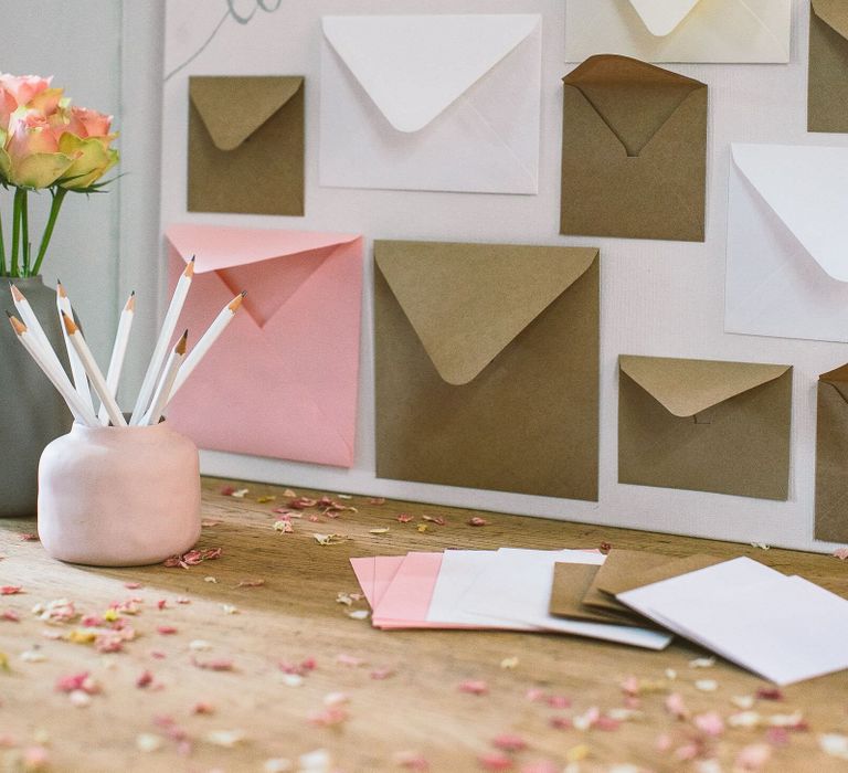 Wedding card table with pencils in a pink pot, roses, a box for guests to leave their cards, and envelopes for guests to leave a love note to the bride and groom