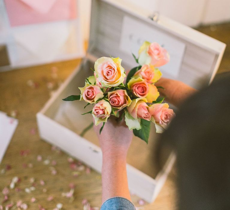 Person putting a bunch of pale pink antique roses into a card box as part of a wedding card table