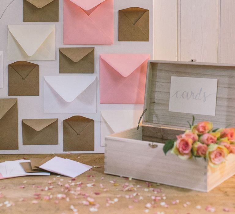 Wedding card table with a box for guests to leave wedding cards, pale pink roses, and a box canvas with envelopes attached to it for guests to leave cards with messages of advice for the bride and groom