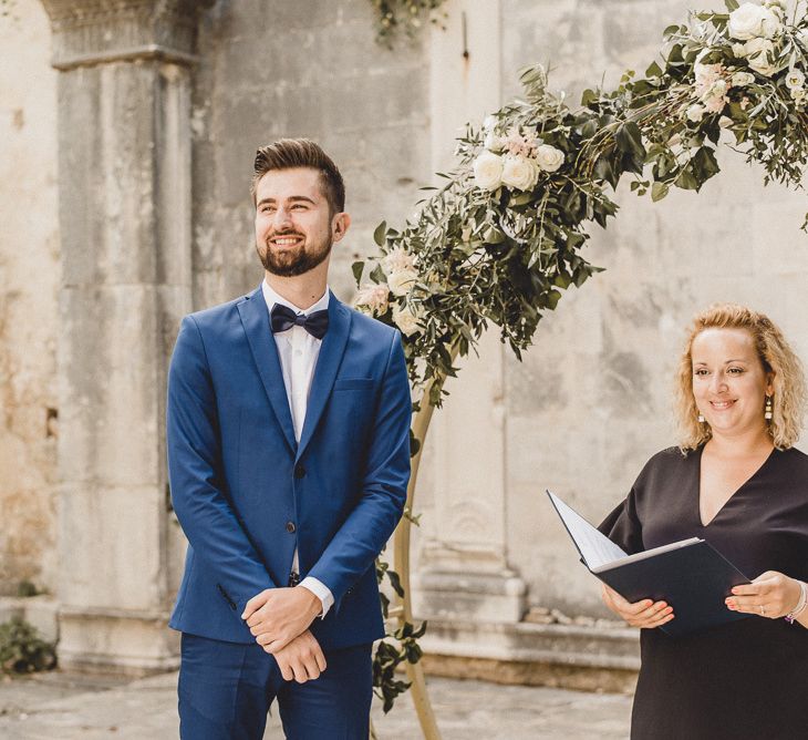 Groom waits for bride in front of floral moon gate