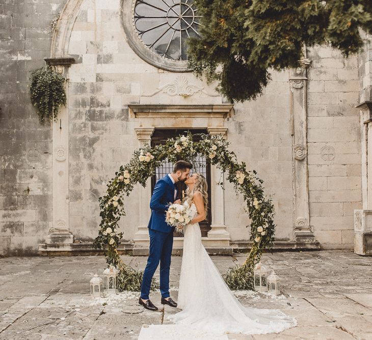 Bride and groom kiss in front of floral moon gate