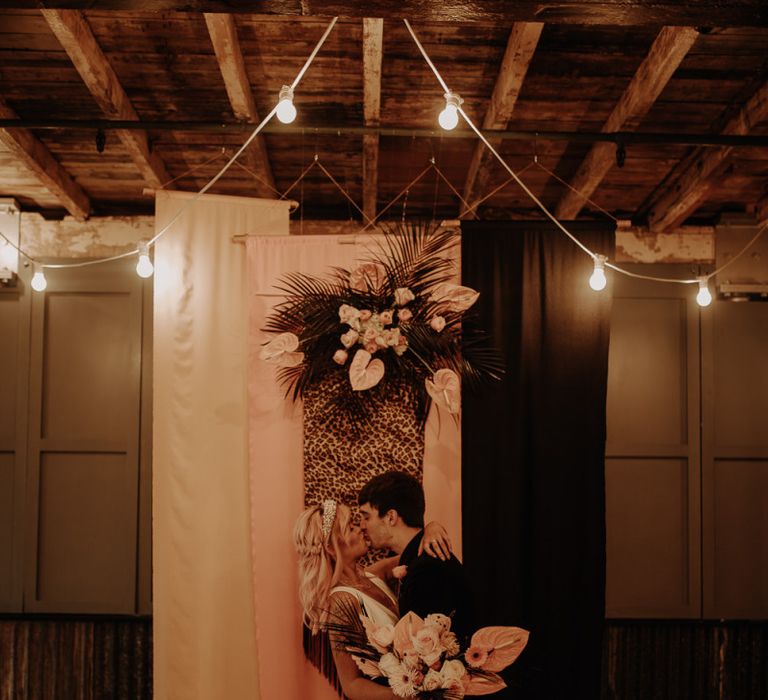 Bride and groom kissing in front of leopard print fabric backdrop