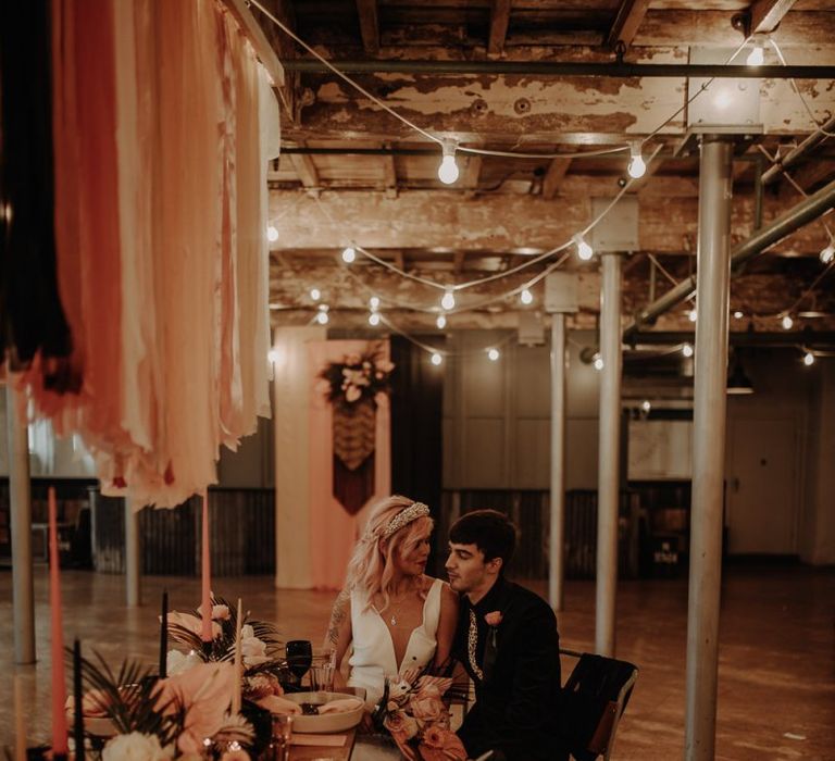 Bride and groom sitting at the table under festoon lights