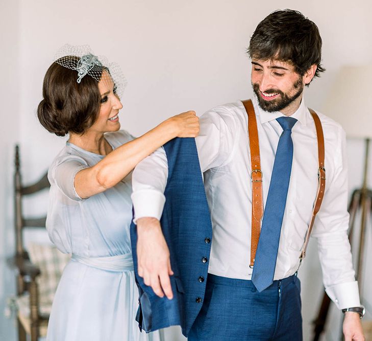 Mother of the bride helping the groom into his navy waistcoat