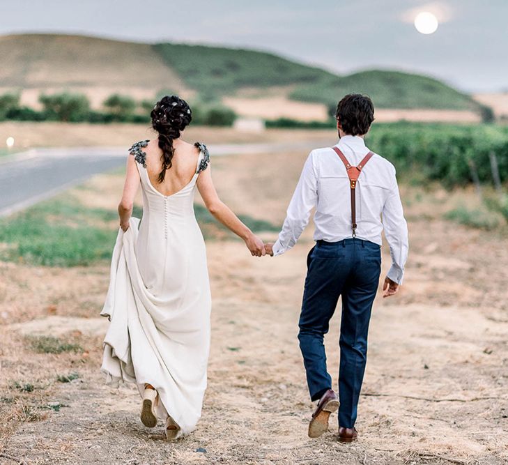 Bride and groom holding hands walking into the sunset