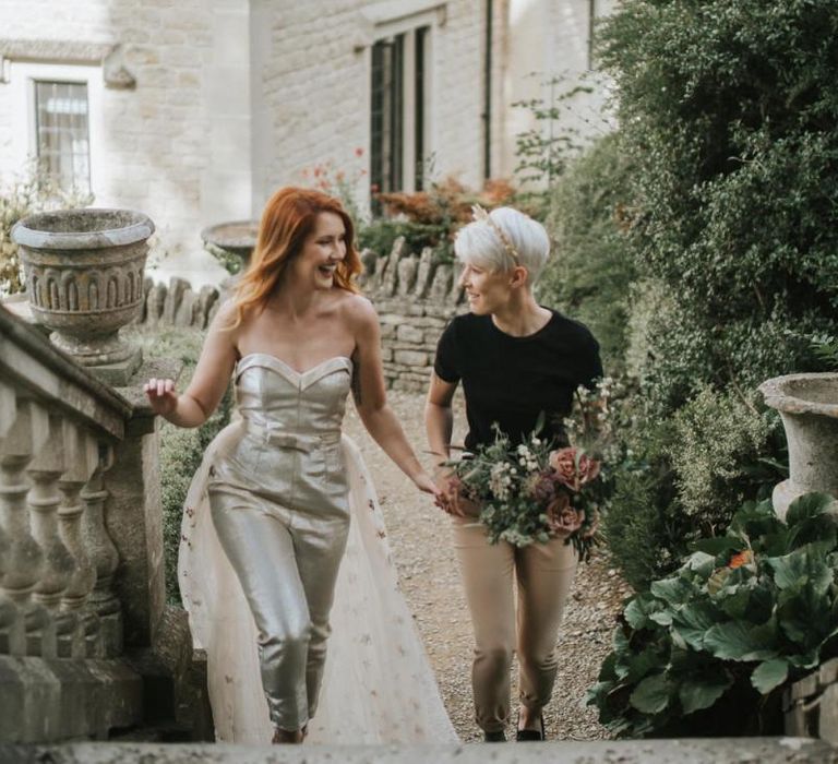 Bride in gold jumpsuit and bride in black t-shirt and beige trousers