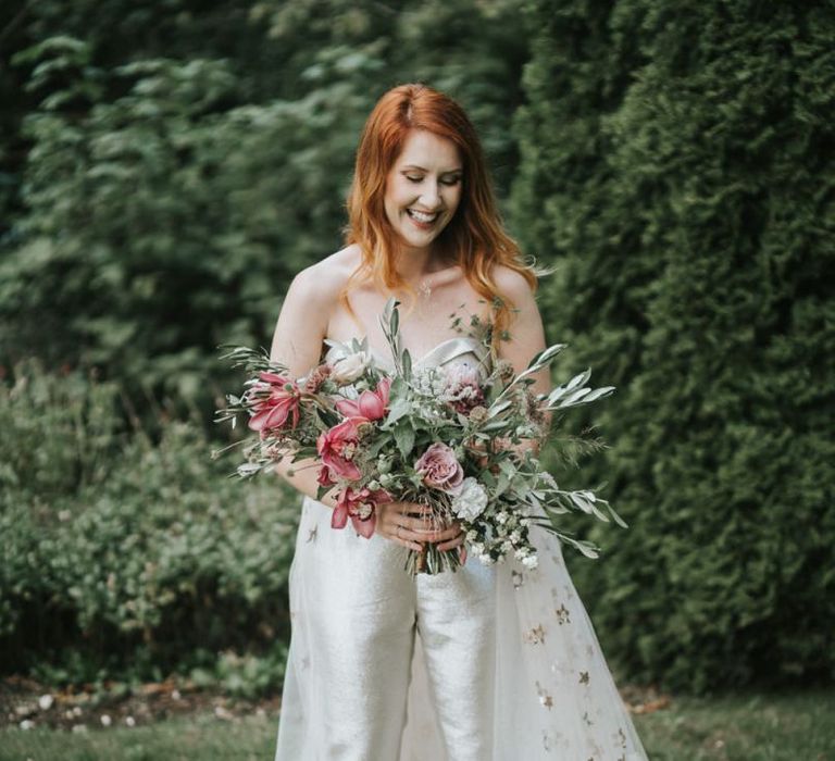 Bride in strapless bridal jumpsuit holding a romantic wedding bouquet